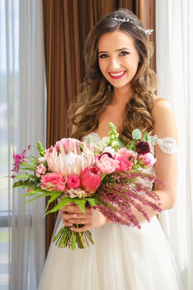 Mireasă cu buchet de protea roz, trandafiri de grădină și amaranthus, la fereastră